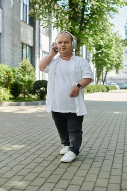 Kapsamlı bir adam şehir caddesinde yürüyor, kulaklıkla müzik dinliyor..