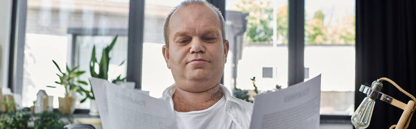 Человек с инклюзивностью сидит у окна, просматривая документы в своем кабинете.