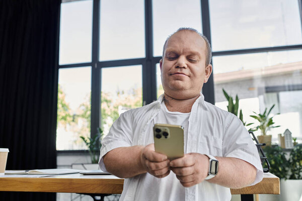 Человек с инклюзивностью сидит в современной офисной обстановке, проверяя телефон.