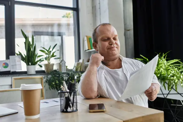 stock image A man with inclusivity sits at a desk reviewing documents in an office.