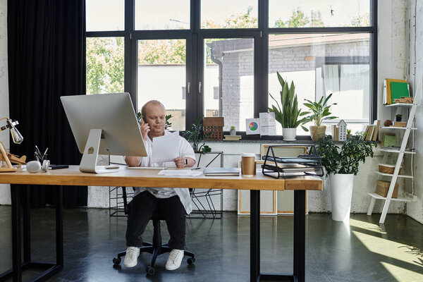 Человек с инклюзивностью сидит за своим столом в офисе и работает за компьютером..