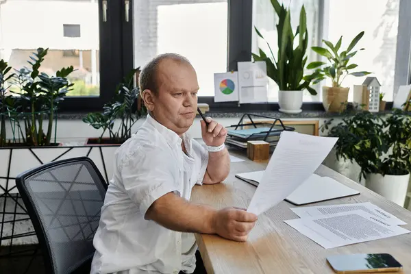 stock image A man with inclusivity sits at a desk in a modern office, reviewing documents.
