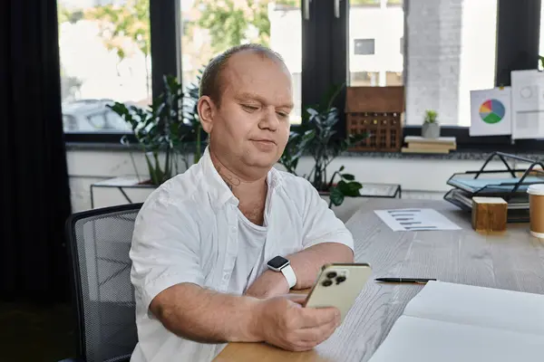 Stock image A man with inclusivity sits at his desk in an office, looking at his phone.