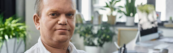 A man with inclusivity, possibly an office worker, thoughtfully looks at the camera.