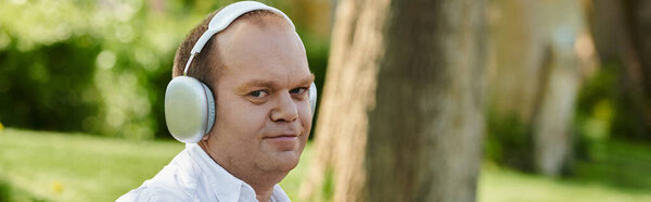 A man with inclusivity wearing headphones walks through a park, enjoying the serenity of nature.