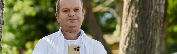 A man with inclusivity with a smartphone stands in a lush park.