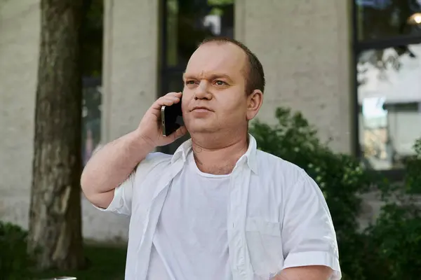 stock image A man with inclusivity in a white shirt talks on his phone outdoors.