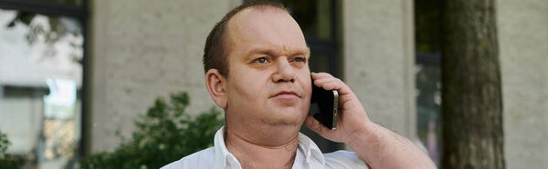 Человек с включённостью в белой рубашке разговаривает по телефону возле здания.