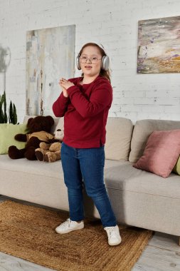 Down sendromlu küçük bir kız oturma odasında kulaklık takıp dans ediyor..