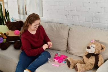 A little girl with Down syndrome plays with her toys on the couch at home. clipart