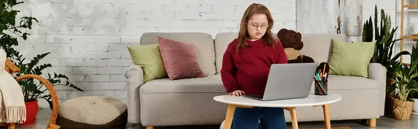 stock image A little girl with Down syndrome uses a laptop at home.