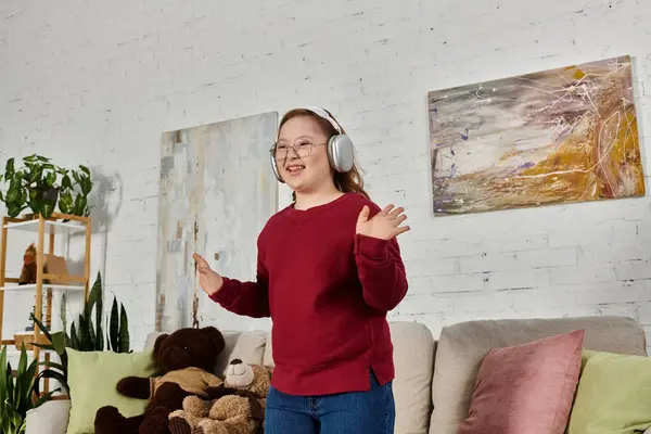 stock image A little girl with Down syndrome dances happily in her living room while wearing headphones.