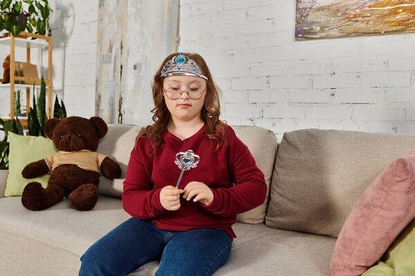 маленькая девочка с синдромом Дауна дома, в короне принцессы и палочке.