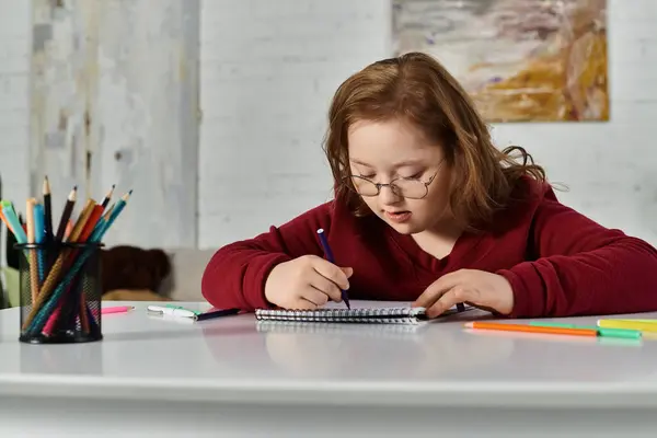 stock image A little girl with Down syndrome concentrates on her artwork at her desk.