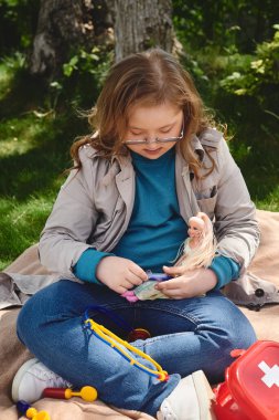 A little girl with Down syndrome plays doctor with her doll outdoors. clipart