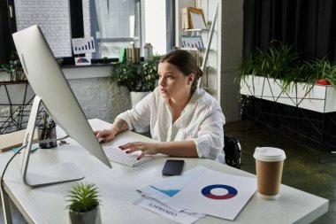 A young businesswoman sits in her wheelchair working at a desk in a modern office. clipart