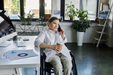 Engelli genç bir iş kadını modern bir ofiste tekerlekli sandalyede oturuyor ve bir telefon görüşmesi yapıyor..