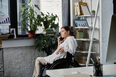 A young woman in a wheelchair uses her phone while working in a modern office. clipart
