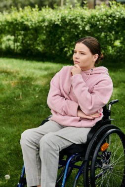 Pembe kapüşonlu genç bir kadın dışarıdaki tekerlekli sandalyede düşünceli bir şekilde oturuyor..
