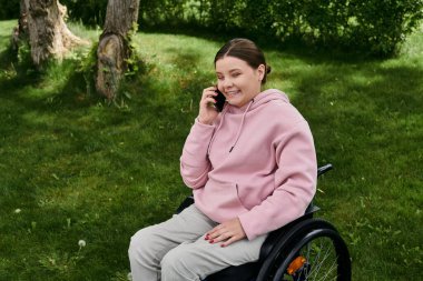 Engelli bir kadın tekerlekli sandalyesinde oturuyor ve telefonla konuşurken gülümsüyor..