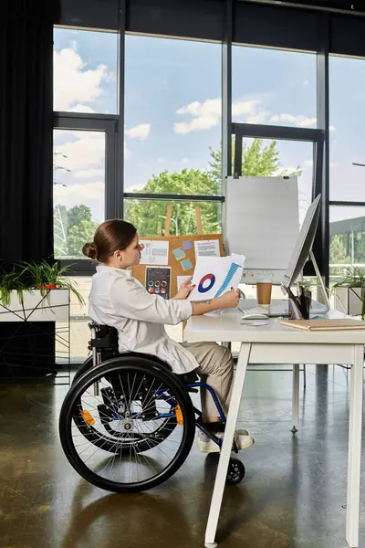 stock image A young businesswoman in a wheelchair works at her desk in a modern office.