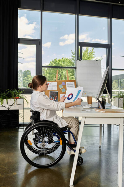 A young businesswoman in a wheelchair works at her desk in a modern office.