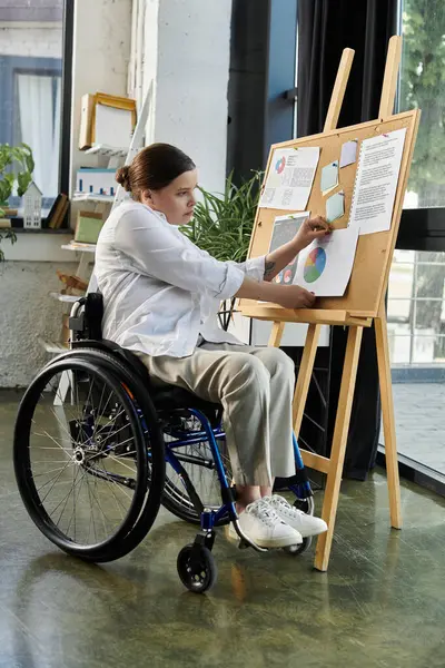 stock image A young businesswoman in a wheelchair works on a project in a modern office setting.