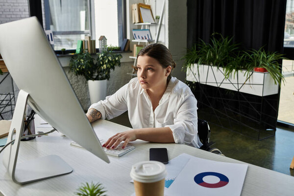 Молодая деловая женщина в инвалидной коляске работает за своим столом в современном офисе.