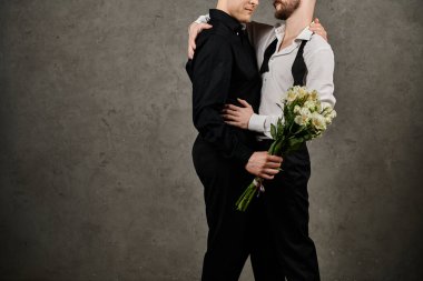 Şık bir eşcinsel çift kucaklaşır, bir buket çiçek tutar, desenli beton bir duvara karşı..