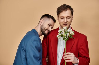 Two men in suits, one with a bouquet of white flowers, share a tender moment. clipart