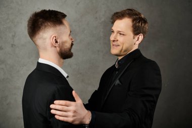 Two men in dapper suits share a tender moment, one gently resting his hand on the others shoulder. clipart