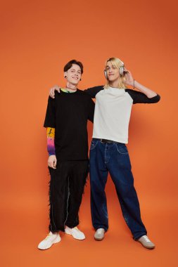 İki genç eşcinsel arkadaş canlı turuncu bir arkaplanda şık bir şekilde poz veriyorlar..