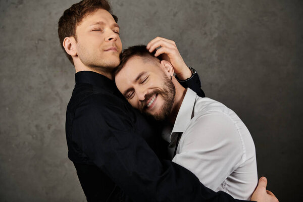 Two men in suits hug each other tenderly in a studio setting.