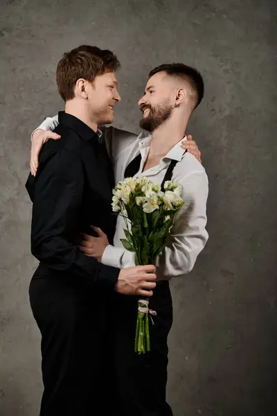 stock image Two men in suits embrace, one holding flowers, gazing lovingly.