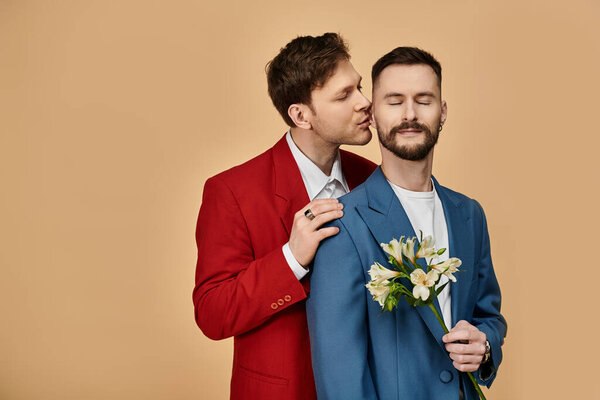 Двое мужчин в элегантных костюмах разделяют нежный момент с цветами.