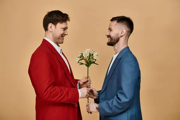 stock image Two men in elegant suits, one holding flowers, looking at each other with affection.