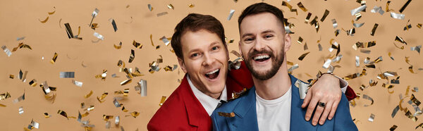 Two men in dapper suits, joyfully embrace amidst falling confetti.