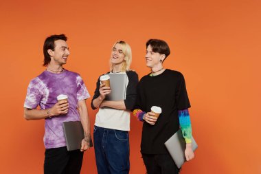 Renkli giyinmiş üç eşcinsel arkadaş turuncu arka planlı bir stüdyoda yan yana dururlar..