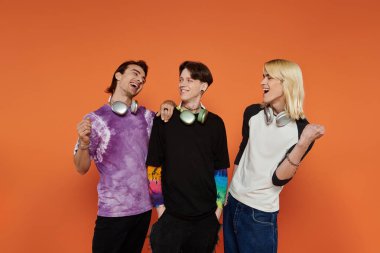 Canlı giyinmiş üç tuhaf arkadaş turuncu bir arka plana karşı poz veriyor, neşe ve dostluk saçıyor..