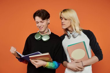 Renkli kıyafetli iki eşcinsel arkadaş turuncu bir arka planda birlikte çalışıyorlar..