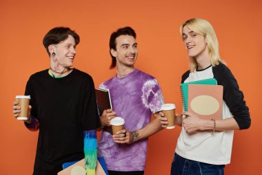 Canlı giyinmiş üç genç arkadaş turuncu bir arka planda birlikte kahve ve sohbetin tadını çıkarıyorlar..