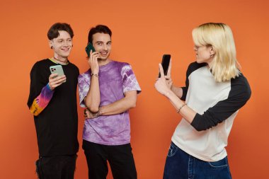 Renkli elbiseli üç eşcinsel arkadaş turuncu arka planda fotoğraf çektirmek için poz veriyor..