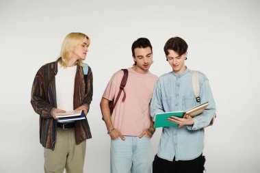 Gri bir arka planda, biri kitap okurken, diğerleri bakınırken, üç gündelik kıyafetli genç yan yana dururlar..