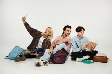 Gri bir arka planda oturan üç genç, gülüyor ve birbirlerine eşlik etmekten zevk alıyorlar..