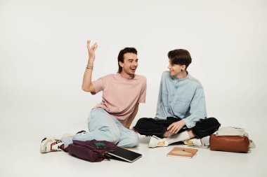 Stüdyoda yerde oturmuş sıradan giyinmiş iki homo öğrenci kahkaha atıyor..