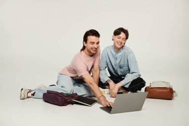 İki genç eşcinsel öğrenci bir stüdyo ortamında dizüstü bilgisayarla iş birliği yapıyor..