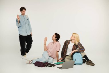 Üç genç öğrenci, günlük giysiler içinde, beyaz bir arkaplanda durup, dostluk ve bağlılık gösteriyorlar..