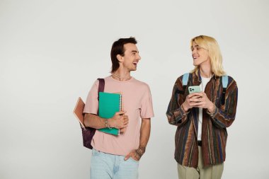 LGBTQIA topluluğunun bir parçası olan iki genç, kitap ve telefon tutarken gülüp sohbet ediyorlar..