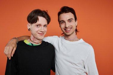 İki genç eşcinsel arkadaş, turuncu arkaplan karşısında canlı bir şekilde poz veriyorlar..
