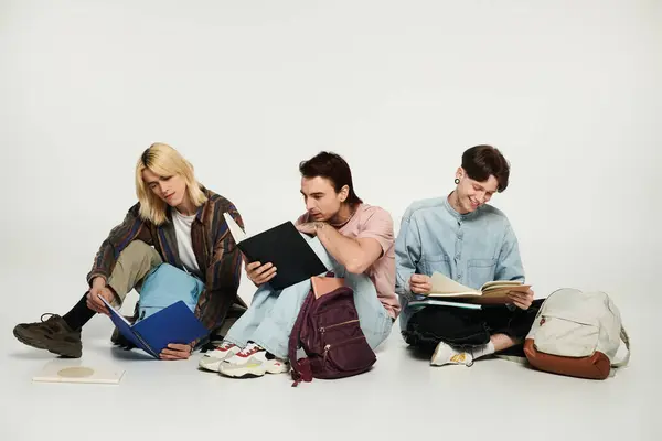 stock image Three young students, part of the LGBTQIA community, sit together on a grey background, studying.